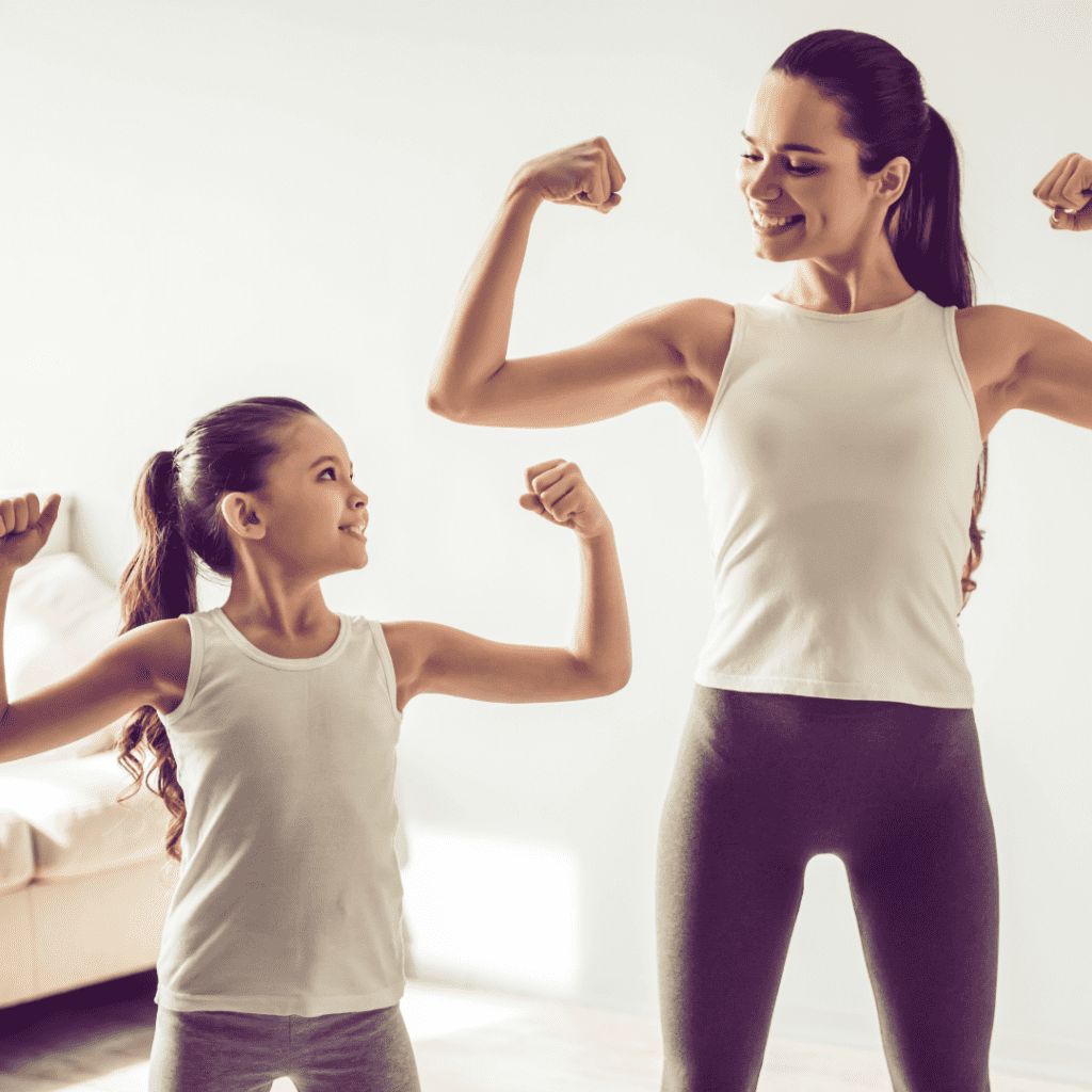 Photograph of a mom and daughter flexing their biceps muscles and smiling at each other.